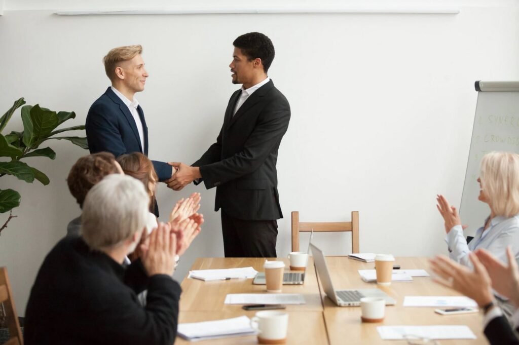 two-businessmen-shaking-hands-at-meeting-with-colleagues-clapping-agreement-partnership-success